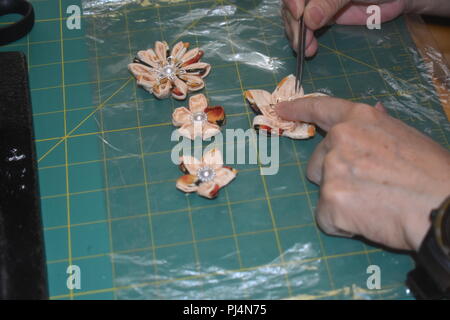 Woman's hands putting final touches on handmade Kanzashi ornamental flowers using kimono material Stock Photo