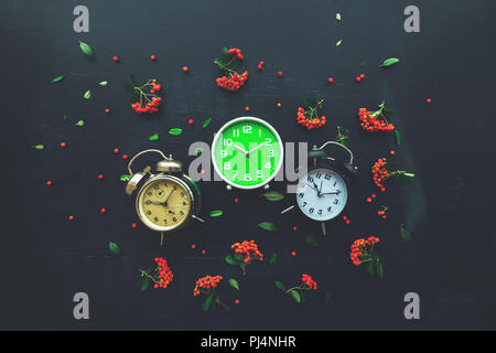 Ten past ten on three different alarm clock, flat lay top view minimal composition of timepieces placed on dark wooden background with decorative wild Stock Photo