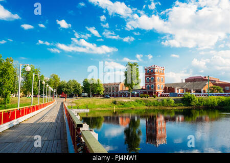 Landscape in summer a bridge across the river on the bank of which is located an old paper factory under a blue sky with cumulus clouds Stock Photo