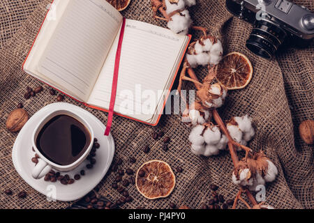 Still life with black coffee retro camera with a branch of cotton and dry orange on a table with burlap and fried coffee beans Stock Photo