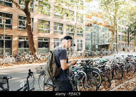 A student with a backpack or a tourist on Leipzig Street in Germany uses a cell phone next to the bicycle parking which is next to the library of the University of Leipig and student hostel. Stock Photo