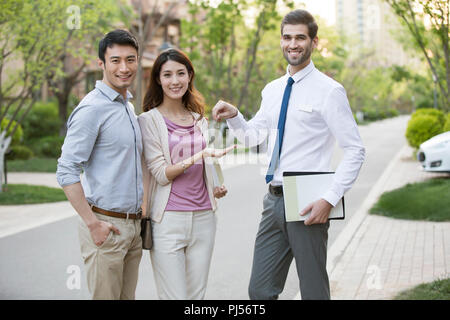 Happy young couple receiving house key from real estate agent Stock Photo