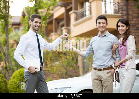Happy young couple receiving car key from car salesperson Stock Photo