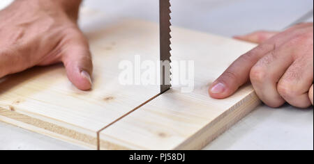 joiner in the workshop saws a wooden board with a sawing machine - detail Stock Photo