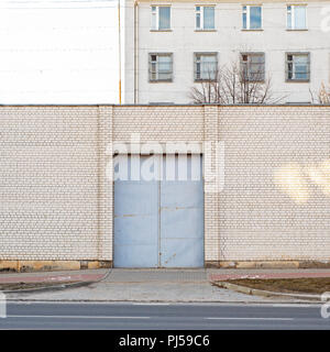 Entrance to abandoned building surrounded by big white brick wall. Industrial background. Stock Photo