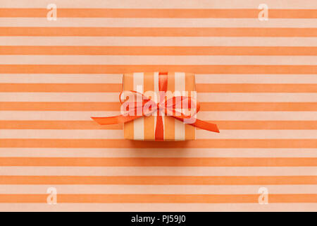 Orange color gift box on orange striped wrapping paper. Minimal geometric background for card, flyer, invitation, placard or voucher. Stock Photo