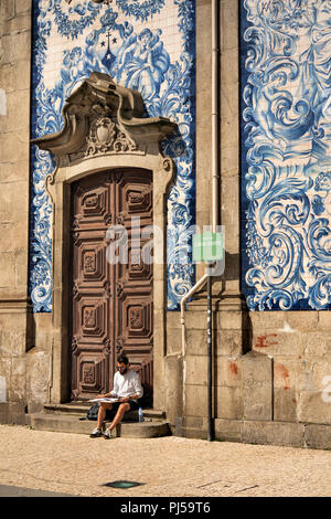 Portugal, Porto, Praça de Carlos Alberto, Igreja do Carmo, baroque catholic church, man sat sketching by door in  tiled wall Stock Photo