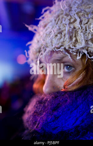 close up of attractive french woman’s face wrapped up warm with blue scarf and wearing a furry cream winter hat at night Stock Photo
