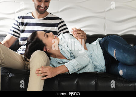 Young latino man and woman holding hands on sofa at home. Happy hispanic couple showing love and romance. Stock Photo