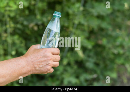 Man's hand taking opened bottle of mineral water against green natural background Stock Photo