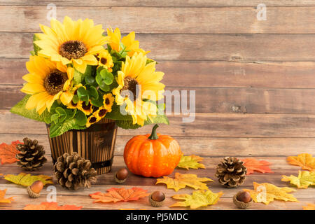 Fall still life with sunflower bouquet in wooden plant pot, pumpkin, leaves, pine cones, and acorns on rustic brown wood panel background. Stock Photo