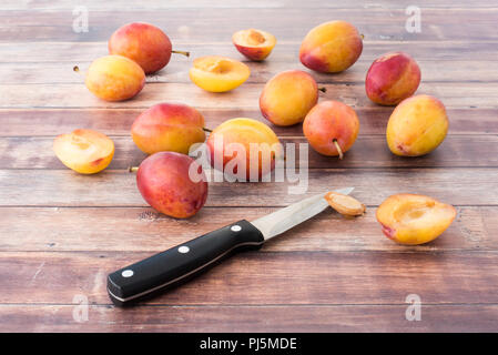 Whole and halved British Victoria plums on dark brown rustic wood panel background. Stock Photo
