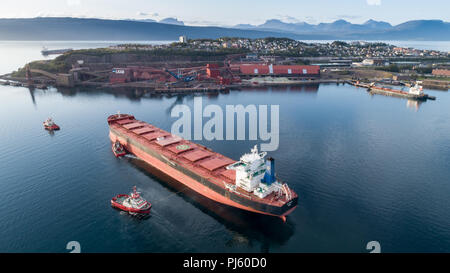 NORWAY,NARVIK - SEPTEMBER 1, 2018:Aerial shot of a cargo ship approaching LKAB port terminal with help of towing ship, Narvik, Norway Stock Photo
