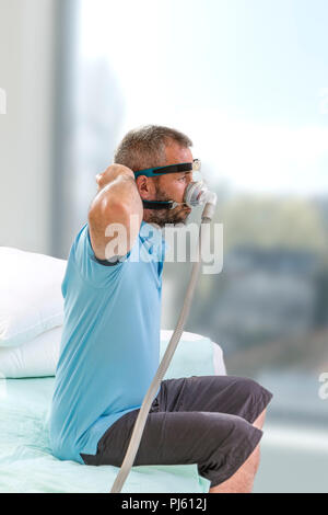 SLEEP APNEA SYNDROME. Man with a sleeping disorder tries on a Cpap for the first time,Man learns to adjust his CPAP equipment, on white Stock Photo