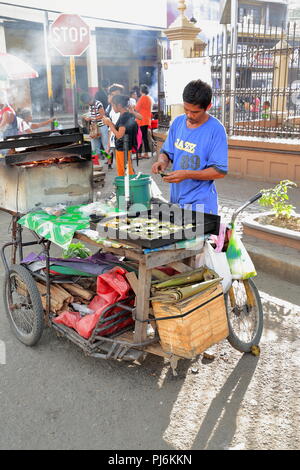 Cebu, Philippines-October 18, 2016: Streetfood salesman cooks and sells Filipino delicacies from her food bicycle-cart fueled by firewood stationed in Stock Photo