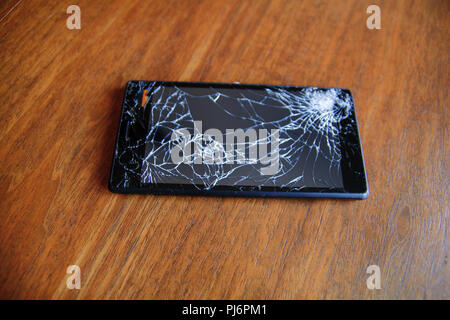 Modern mobile smart phone display with broken cracked glass screen on a wooden table, close up. Stock Photo