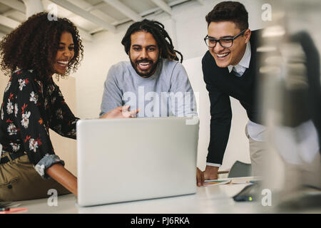 Business colleagues looking at a laptop computer and laughing. Office mates enjoying their work and having fun in office. Stock Photo