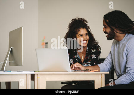 Smiling businessman and woman discussing work sitting at the desk with laptop and a desktop computer. Smiling businesswoman talking to her colleague a Stock Photo