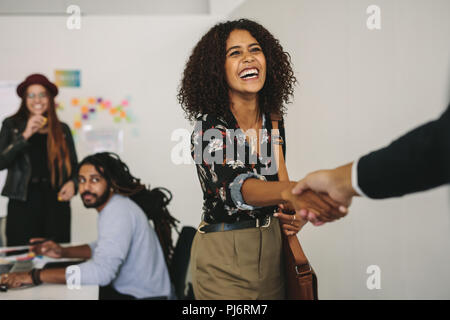 Happy business professional wearing office bag shaking hands with client. Business partners in a meeting while a businesswoman greets a customer. Stock Photo