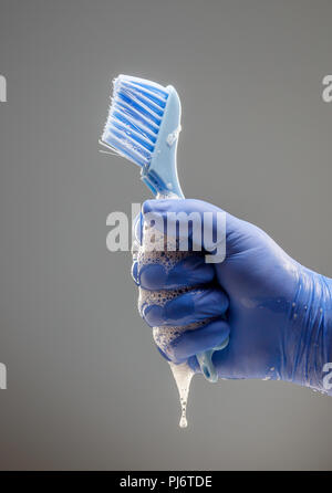 A man's hand in a blue glove holds a brush for cleaning with a dripping foam Stock Photo