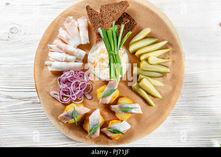 Sandwich on fried potatoes with herring, green onion. Tasty appetizer with sauerkraut, pickled cucumber, mustard on wooden Board. Rye bread and lard Stock Photo