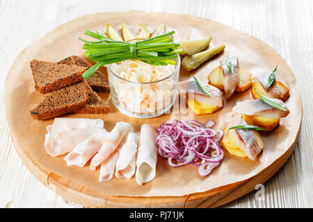 Sandwich on fried potatoes with herring, green onion. Tasty appetizer with sauerkraut, pickled cucumber, mustard on wooden Board. Rye bread and lard Stock Photo