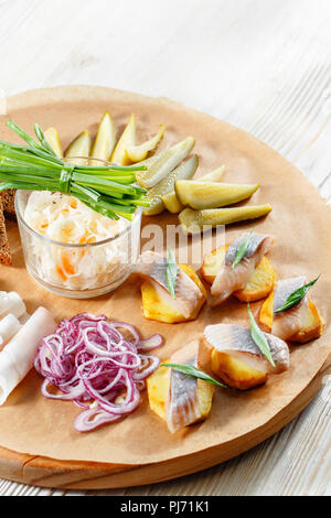 Sandwich on fried potatoes with herring, green onion. Tasty appetizer with sauerkraut, pickled cucumber, mustard on wooden Board. Rye bread and lard Stock Photo