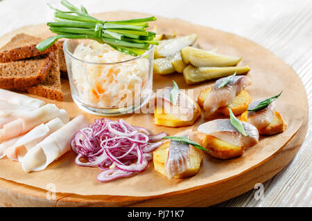 Sandwich on fried potatoes with herring, green onion. Tasty appetizer with sauerkraut, pickled cucumber, mustard on wooden Board. Rye bread and lard Stock Photo