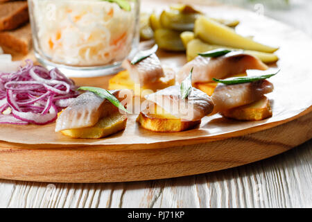 Sandwich on fried potatoes with herring, green onion. Tasty appetizer with sauerkraut, pickled cucumber, mustard on wooden Board. Rye bread and lard Stock Photo