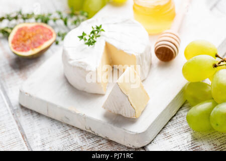 Camembert or brie cheese with grapes, figs and honey on white wooden serving board. Closeup view, selective focus Stock Photo