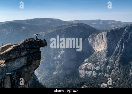 A sits on an overhanging rock at Glacier Point enjoying the breathtaking view of Yosemite Valley, California, USA. Stock Photo