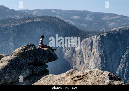 A sits on an overhanging rock at Glacier Point enjoying the breathtaking view of Yosemite Valley, California, USA. Stock Photo