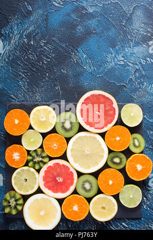 Fruits rich in vitamin C: oranges, lemons, kiwis, grapefruits and limes on the black slate on the dark blue background, top view Stock Photo