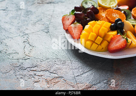 Sliced fruits and berries on white plate on the grey stone background, copy space, selective focus Stock Photo