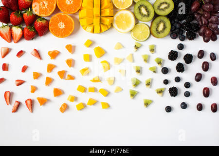 Top view of whole fruits and cut slices in the rows; red, orange, yellow, green fruits with cut pieces on the white background; grapefruit, mango, str Stock Photo