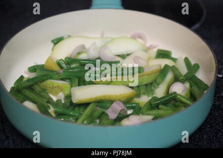 Sliced pear, chopped broccoli, and sliced red onion in a pan.  Searing ingredients on a flat top oven. Stock Photo