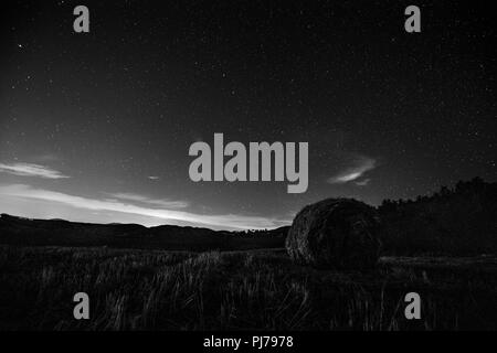 Beautiful view of starred night sky with clouds over a cultivated field with hay bale Stock Photo