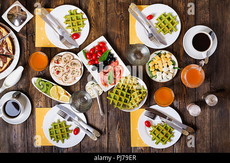 Breakfast food table. Festive brunch set, meal variety with spinach waffles, salmon, cheese, olives, chicken rolls and cheesecake. Top view. Flat lay Stock Photo