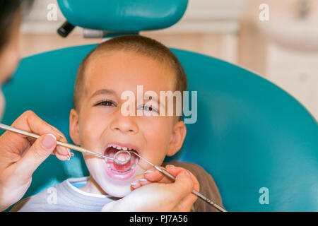 Pediatric dentist examining a little boys teeth in the dentists chair at the dental clinic. Dentist examining little boy's teeth in clinic. Stock Photo