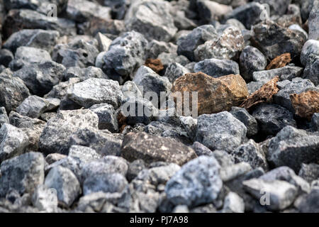 stones average size mostly dark gray and several red, on the ground, texture, background, photo in the street in daylight, close-up Stock Photo