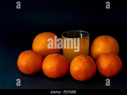Group of mandarins, tangerine fruits, two oranges isolated on black with a glass of juice. Stock Photo