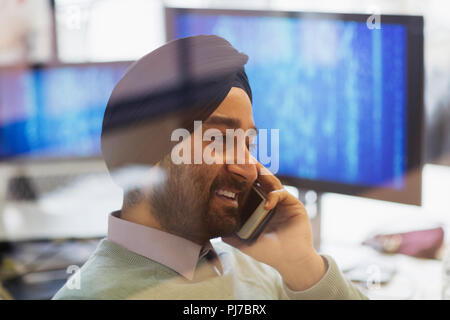 Indian computer programmer in turban talking on smart phone in office Stock Photo