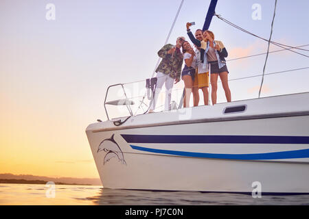 Friends with smart phone taking selfie on catamaran at sunset Stock Photo