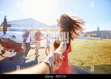 Personal perspective woman leading man by hand toward prop airplane Stock Photo