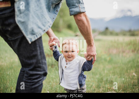 Father walking with baby son in grassy field Stock Photo