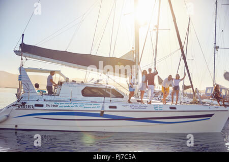 Portrait friends waving on catamaran in sunny harbor Stock Photo