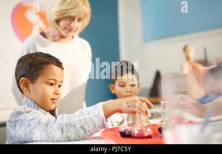 Teacher watching curious students playing with beakers at interactive exhibit in science center Stock Photo
