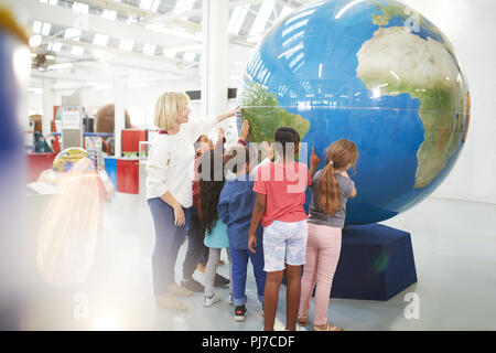 Teacher and students touching large globe in science center Stock Photo