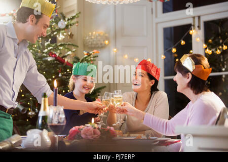 Multi-generation family in paper crowns toasting champagne flutes at candlelight Christmas dinner Stock Photo