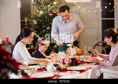 Multi-generation family carving Christmas turkey at candlelight dinner table Stock Photo